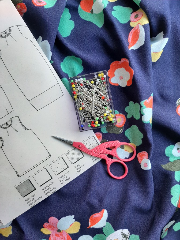 Floral viscose fabric with a Burda sewing pattern, pack of glass-head pins and a pair of pink embroidery scissors